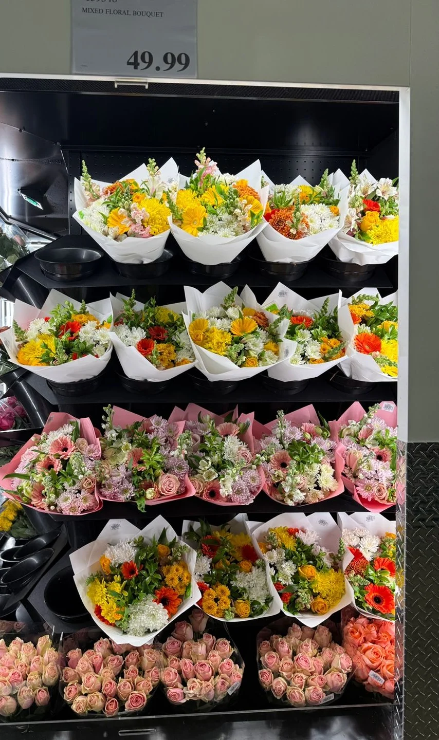 코스트코 꽃 진열대. 위에 MIXED FLORAL BOUQUET 49.99 가격표가 있고 흰 종이와 분홍 종이로 싼 꽃다발이 네 단으로 놓여 있다