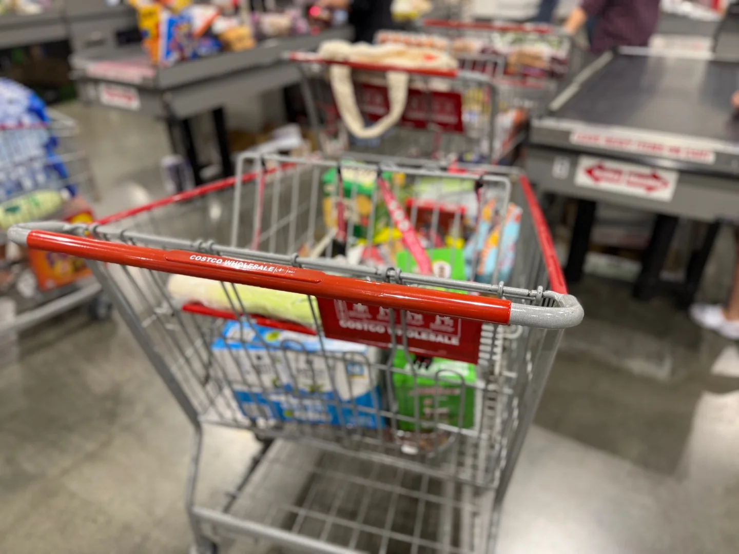 계산대 앞에 선 코스트코 카트. 빨간 손잡이에 COSTCO WHOLESALE 글자가 보이고 뒤쪽 계산대는 흐리게 찍혔다
