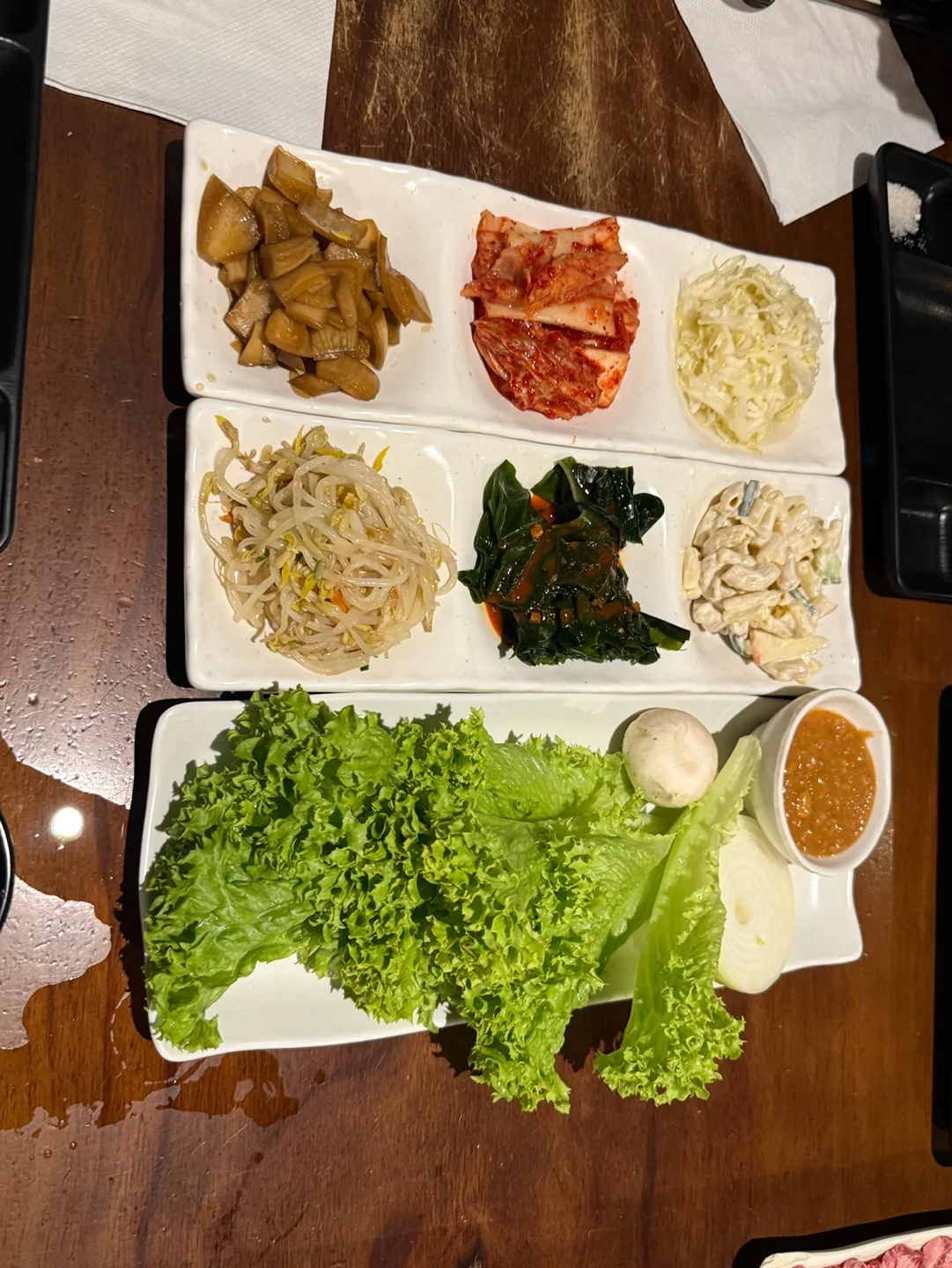 세 칸짜리 흰 접시 두 개에 담긴 반찬 여섯 가지와 상추, 쌈장, 양송이버섯, 양파가 담긴 쌈 접시