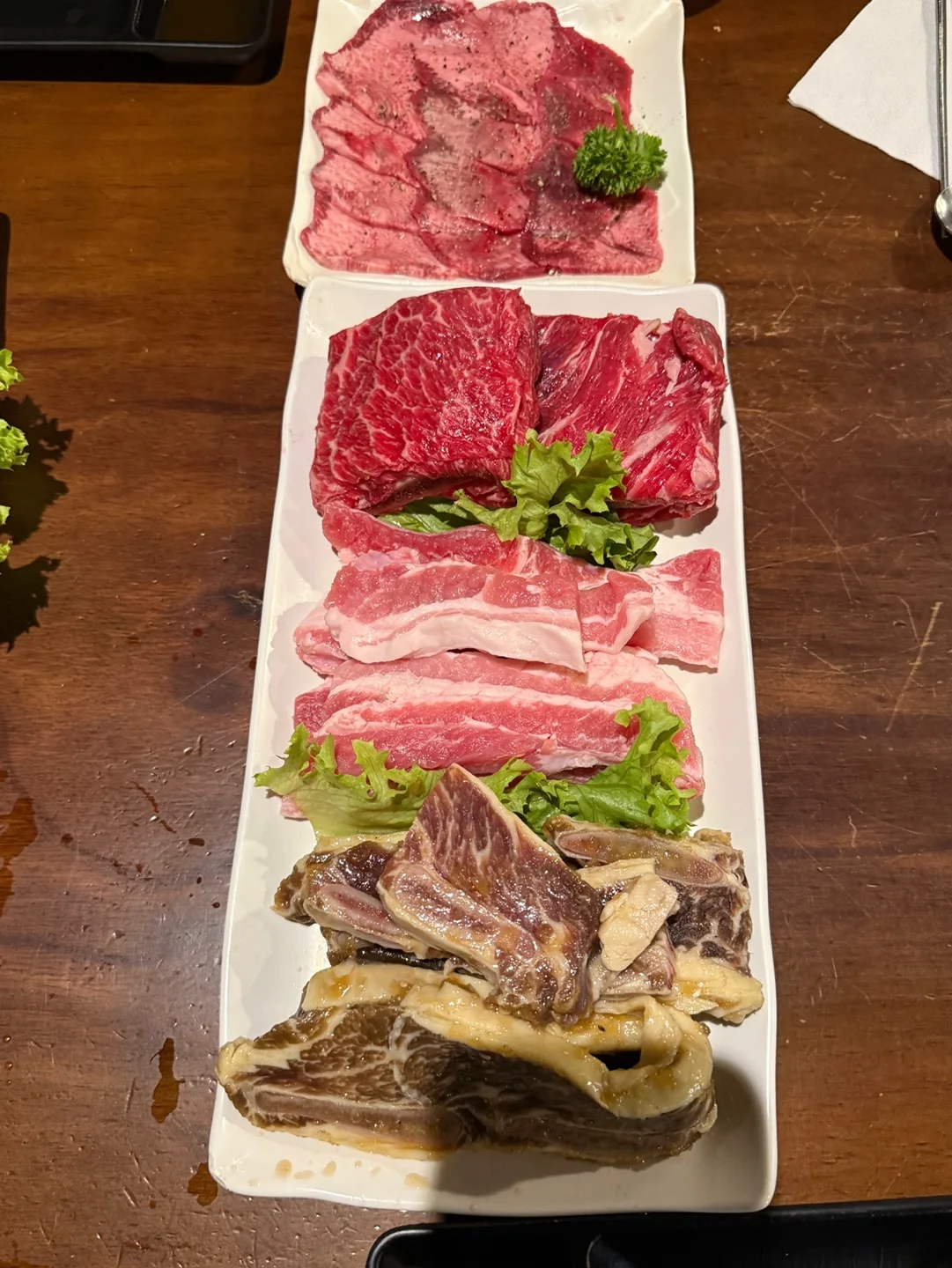 긴 흰 접시에 생갈비, 생삼겹살, 양념에 재운 LA갈비가 차례로 담겨 있고 위쪽 작은 접시에 얇게 썬 우설이 있다