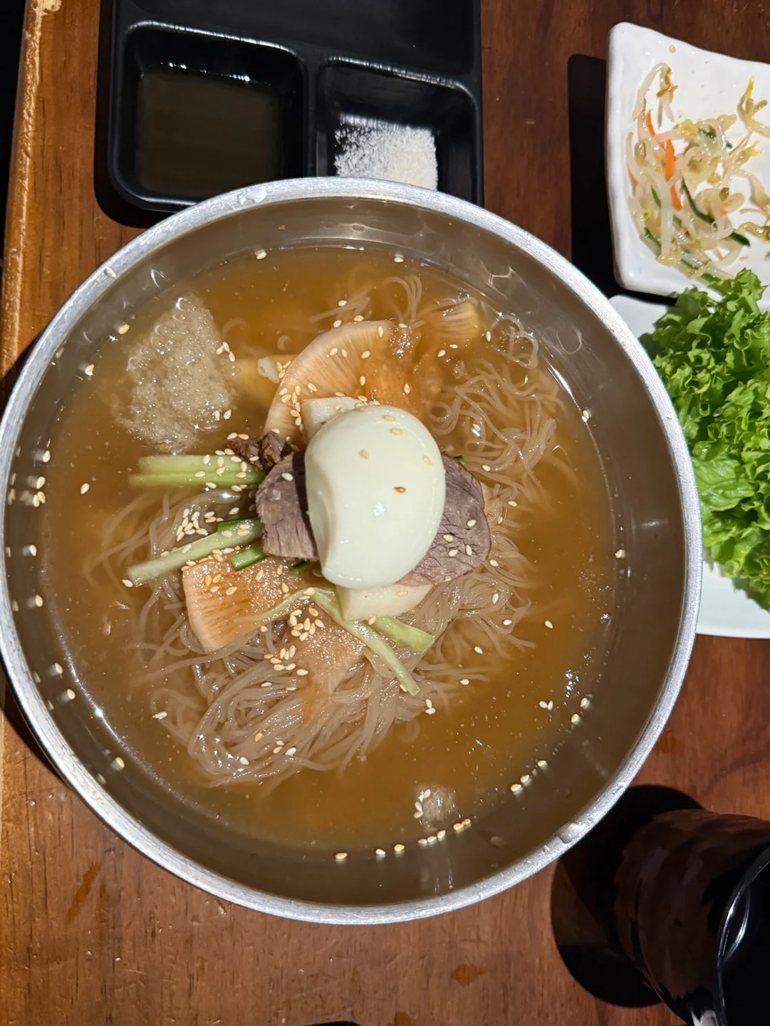 스테인리스 그릇에 담긴 물냉면. 살얼음 육수 위에 삶은 달걀 반쪽, 고기, 무, 오이가 올라가 있다
